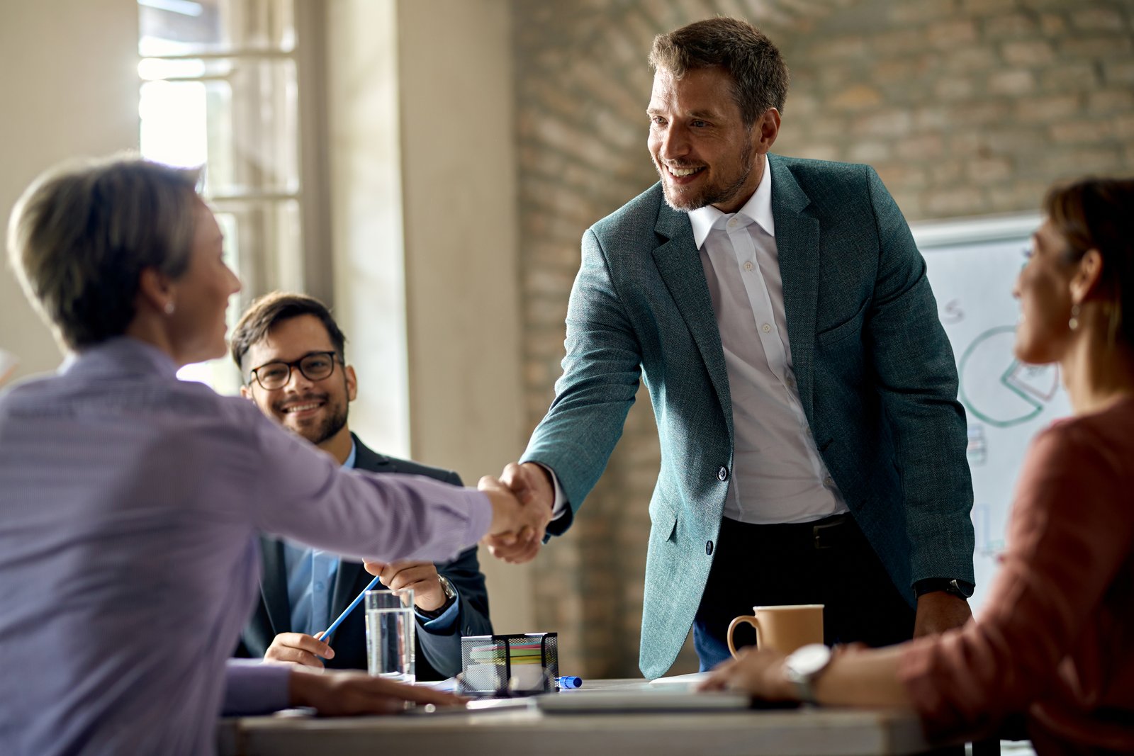 Two business professionals shaking hands in a meeting, symbolizing reliable delivery and proven results for clients.